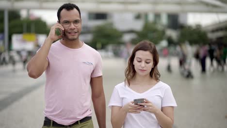 Front-view-of-two-people-walking-on-street-with-smartphones