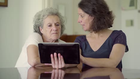 Two-women-sitting-at-table-and-using-tablet.