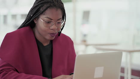 Afro-American-attractive-young-girl-with-plump-rose-lips-and-braids-in-aviator-eyeglasses-wearing-rose-coat-working-on-laptop-outside