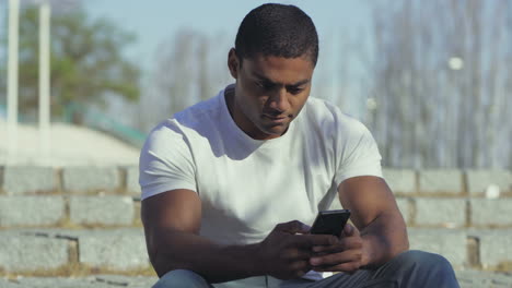 Focused-African-American-man-using-smartphone-outdoor.