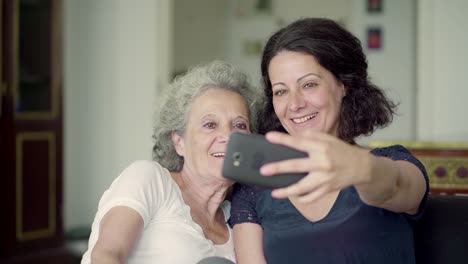 Daughter-and-mother-having-video-chat-on-phone,-greeting-on-sofa