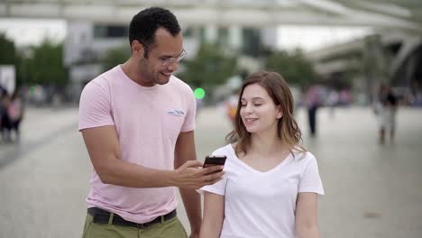 Smiling-young-couple-walking-on-street-and-looking-at-phone