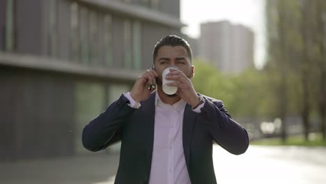 Man-talking-by-smartphone-and-drinking-from-paper-cup-outdoor