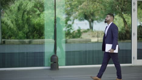 Handsome-bearded-businessman-walking-with-laptop-on-street