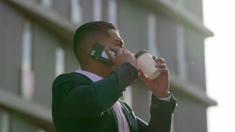 Man-drinking-from-paper-cup-and-talking-by-smartphone