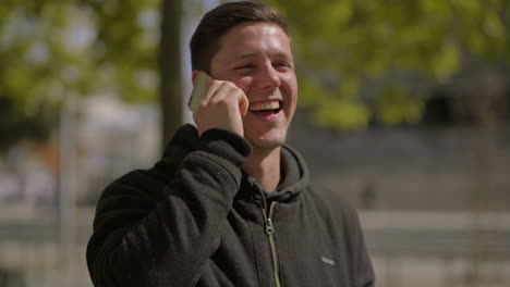 Man-talking-by-smartphone-and-laughing-outdoor