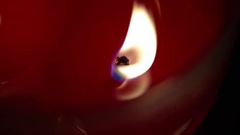 Candle-wick-burns-flickering-glowing,-spreading-light-across-red-surface,-slow-motion