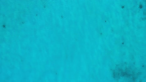 White-sand-shimmers-below-shallow-ocean-water,-drone-ascends-into-sky