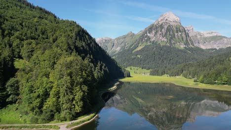 Un-Lago-Cristalino-Como-Un-Espejo-Refleja-La-Naturaleza-Verde-Del-Bosque-De-Pinos-De-Alta-Montaña-De-Los-Alpes-Rocosos-En-Las-Tierras-Altas-Alpinas-Escénicas-De-Suiza-Con-Un-Montón-De-Maravilloso-Fondo-Natural-Día-Soleado-En-Verano