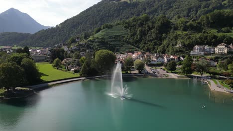 Aerial-viewing-circling-a-fountain-in-the-middle-of-a-lake-in-a-resort-town-in-the-mountains