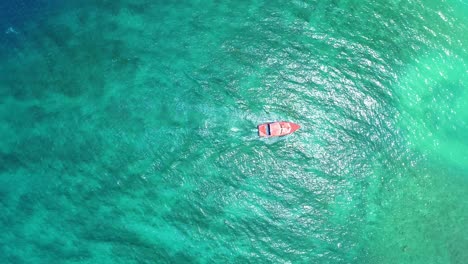 Red-boat-turns-slowly-in-shallow-sandy-coral-reef-water,-drone-top-down-static