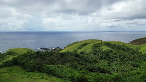 Vista-Aérea-Cinematográfica-De-Impresionantes-Colinas-Cubiertas-De-Selva-Frente-A-Aguas-Cristalinas-Del-Océano-Y-Nubes-En-La-Isla-De-Catanduanes,-Filipinas