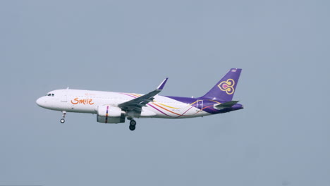 Airbus-of-Thai-Smile-Airways-almost-landing-revealing-an-air-traffic-control-tower-in-the-background-at-Suvarnabhumi-Airport-in-Bangkok,-Thailand-with-its-wheels-down-as-a-bird-flies-by