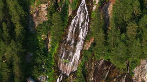 Majestic-aerial-shot-of-beautiful-waterfall-surrounded-by-pine-trees-in-alps