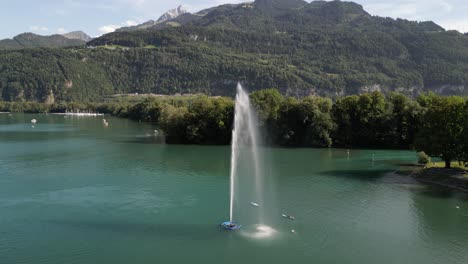 Static-drone-shot-of-a-fountain-in-the-middle-of-lake-in-a-mountain-valley