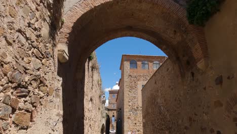 Picturesque-Old-town-in-Caceres,-Tilt-down-shot-from-antique-archway-to-narrow-street,-Spain