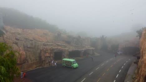 Ascending-aerial-shot-of-green-coach-vehicle-and-tourists-in-foggy-and-bad-rainy-weather-condition