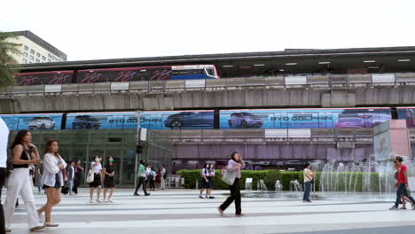 Menschen-Sind-Damit-Beschäftigt,-Außerhalb-Von-Siam-Paragon-In-Bangkok-Mit-Dem-BTS-Bahnhof-Spazieren-Zu-Gehen,-An-Dem-Züge-Abfahren-Und-Für-Passagiere-Halten,-Thailand