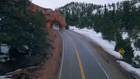 Carretera-Asfaltada-Con-Una-Formación-De-Roca-Roja-De-Arco-única-En-El-Parque-Nacional-Bryce-Canyon-En-Utah,-EE.UU.