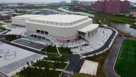 Toma-Aérea-De-Establecimiento-Con-Plataforma-Rodante-Hacia-Atrás-Del-Hermoso-Centro-Olímpico-De-Weihai-Con-Campo-De-Fútbol-En-China-Con-Vista-A-Edificios-De-Arquitectura-Clásica-China