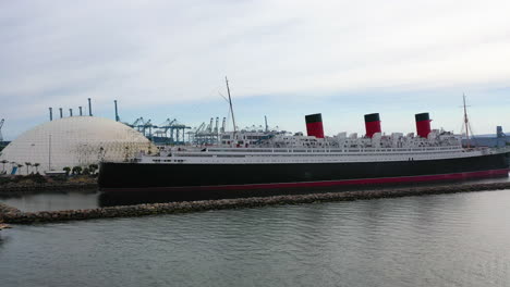 Drone-shot-in-front-of-the-Queen-mary-ship-docked-in-cloudy-Los-Angeles,-USA