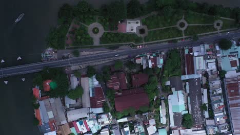 Top-down-Aerial-view-on-Kenh-Te-canal-Ho-Chi-Minh-City-with-old-iron-and-wood-shacks,-traditional-river-boats-and-ultra-modern-high-rise-buildings,-bridge-traffic-and-landscaped-park