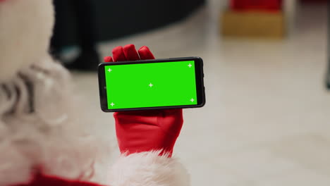 Staff-assistant-in-festive-decorated-fashion-boutique-dressed-as-Santa-Claus-holding-chroma-key-smartphone,-browsing-through-clothing-store-ecommerce-website,-inputting-promotional-xmas-sales-online
