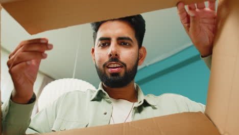 Happy-Indian-man-shopper-unpacking-cardboard-box-delivery-parcel-online-shopping-purchase-at-home