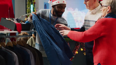 Retail-assistant-in-xmas-ornate-clothing-store-helping-senior-couple-during-their-Christmas-frenzy-shopping-spree.-Worker-offering-advice-to-older-clients-during-winter-holiday-season