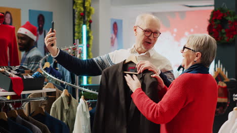 Cheerful-elderly-couple-shopping-for-clothes-while-on-online-videocall-with-son,-helping-them-pick-perfect-Christmas-gift-before-festive-family-dinner-visit-during-winter-holiday-season