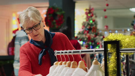 Elderly-woman-browsing-through-clothes-in-xmas-adorn-clothing-store-during-winter-holiday-season.-Senior-client-in-shopping-spree-session-at-Christmas-decorated-fashion-boutique-in-mall