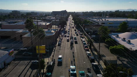 Drone-shot-tilting-over-old-cars-driving-on-the-streets-of-sunny-Los-Angeles,-USA