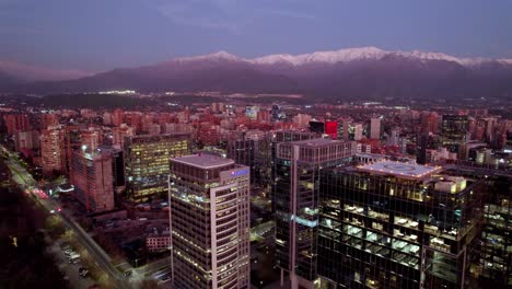 Dolly-in-aerial-view-of-the-modern-buildings-of-Nueva-Las-Condes-in-Santiago-Chile,-business-center-of-the-upper-district-of-the-city,-skyline-with-snow-capped-mountains