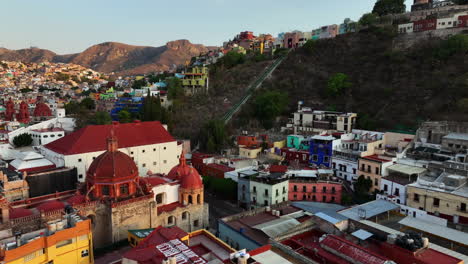 Aerial-view-rising-over-the-cityscape,-toward-Guanajuato-Funicular-to-the-El-Pipila-Statue,-sunset-in-Mexico