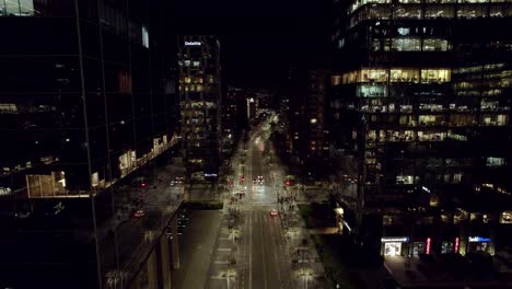 Aerial-dolly-out-view-of-a-street-illuminated-at-night-with-cars-and-pedestrians,-person-on-scooter-to-be-environmentally-friendly,-Santiago-Chile