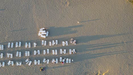 Drone-top-down-view-of-sunbeds-on-a-sandy-beach-at-sunset