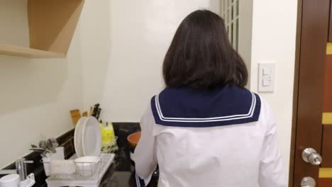 Static-back-view-of-Asian-schoolgirl-in-uniform-checking-the-time-while-cooking-in-kitchen