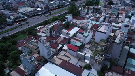 Die-Drohne-Neigt-Sich-Von-Den-Dächern-Des-Dicht-Besiedelten-Industrie--Und-Wohngebiets-Von-Ho-Chi-Minh-Stadt-In-Vietnam-Zu-Einem-Weiten-Panorama-Mit-Modernen-Wohnhochhäusern-Und-Einer-Hauptstraße-In-Der-Sonne