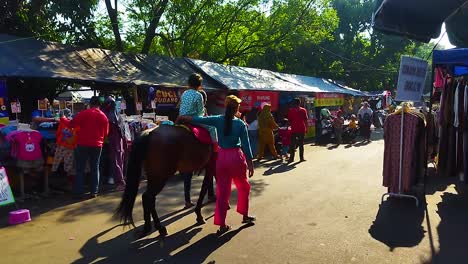 Ein-Kleines-Kind,-Das-Einen-Traditionellen-Überraschungsmarkt-Oder-Einen-Autofreien-Tag-In-Indonesien-Besucht,-Reitet-Mit-Einem-Lehrer-Und-In-Begleitung-Seiner-Mutter-Auf-Einem-Pferd