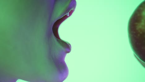 Extreme-close-up-of-a-woman-lip-from-the-side-while-she-takes-a-pleasurable-bite-of-a-red-apple-in-front-of-green-background-in-slow-motion