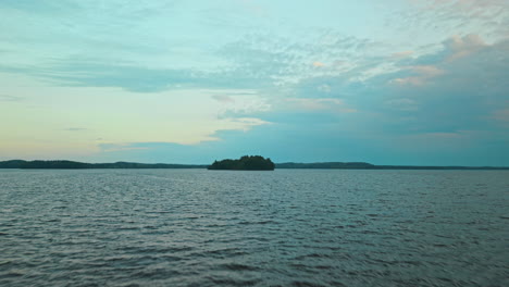 Lake-and-island-or-isle-landscape-in-southern-Finland,-camera-approaching-fast-and-close-to-water,-then-climbing-to-top-shot-of-the-island