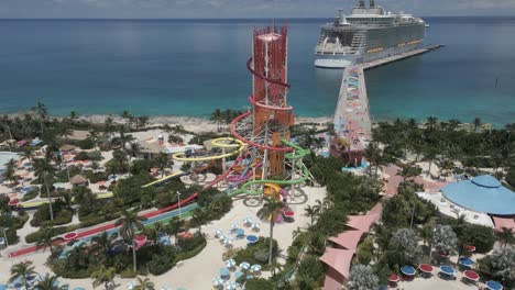 Aerial-rises-above-colorful-waterpark-on-Coco-Cay,-cruiseship-at-pier