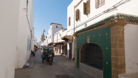 El-Hombre-En-Scooter-De-Entrega-Navega-Por-La-Bulliciosa-Calle-De-La-Medina-De-Rabat-Con-Puertas-Vibrantes,-Marruecos