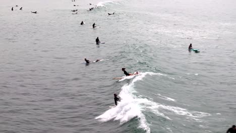 Aerial-view-of-woman-surfer-catching-a-wave,-with-multiple-others-on-surfboards-in-the-water