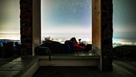 Filmischer-Zeitraffer-Einer-Schlafenden-Person,-Während-Sie-Einen-Zeitraffer-Von-Sternen-über-Dem-Himmel-Einer-Stadt-Fotografiert