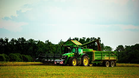 Cinematic-time-lapse-of-a-tractor-and-a-harvester-conducting-work-on-a-field-with-trees-in-the-background