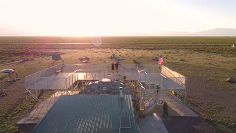 Couple-standing-on-top-of-the-UFO-Watchtower-watching-the-sunrise,-aerial