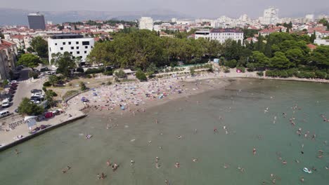 Aerial---Bacvice-Beach,-Split:-bustling-crowd-near-shoreline,-Adriatic-Sea-ambiance