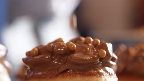 Chocolate-ferrero-donut-being-covered-with-caramel-pieces-side-view