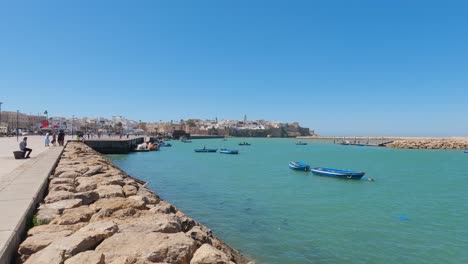 Serena-Orilla-Del-Río-Rabat:-Barcos-Atracados,-Lugareños-Disfrutando-Del-Ambiente-Marítimo